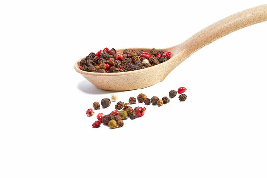 Mixture of peppers in a wooden spoon and scattered balls of pepper on a white background, seasonings, spices, kitchen