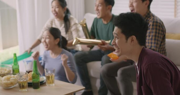 Group of young adult friend man and woman asia people sit at sofa couch joy chanting party fun game match world cup live TV at home eat snack bowl drink beer bottle glass jump mad happy win exult face