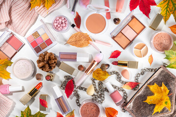 Obraz na płótnie Canvas Autumn make up set on white table background, with autumn leaves and beauty accessories. Various makeup professional cosmetics on white table background with fall cozy sweater and woman handbag