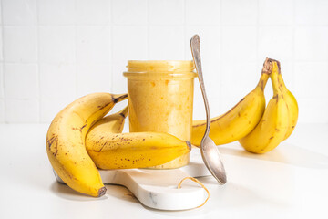 Bananas jam in small glass jar with fresh bananas on  white table background 