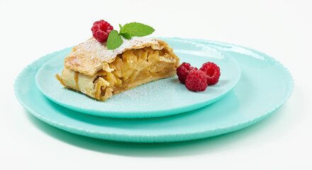 Slice of apple strudel on a round plate, white background