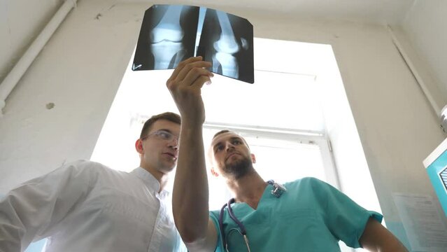 Male medics consult with each other while looking at x ray image. Two caucasian doctors view mri picture and discussing about it. Medical workers in hospital examine x-ray prints. Close up