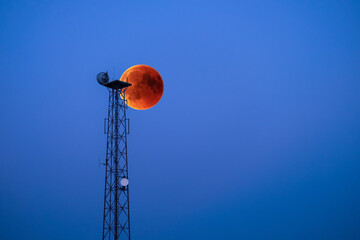 low angle view of blood moon behind communications tower against clear blue sky - Powered by Adobe
