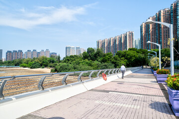 Man walking along coastal promenade with high-rise buildings in the background.