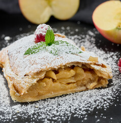 Baked strudel with apples sprinkled with powdered sugar on a black board
