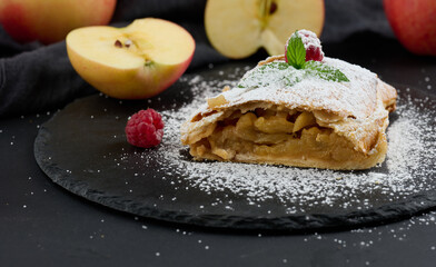 Baked strudel with apples sprinkled with powdered sugar on a black board