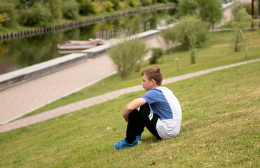 boy teenager sits on the river bank in a big city in summer