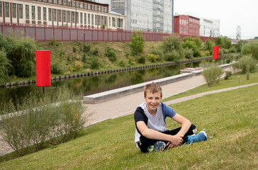 Fototapeta premium boy teenager sits on the river bank in a big city in summer
