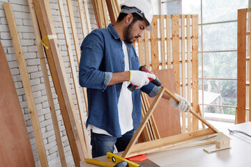 A carpenter uses an electric light to drill into a wooden plank. carpentry concept.