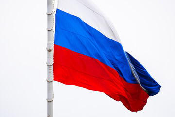 The state symbol of the Russian Federation in the wind. A large Russian flag against a blue sky with clouds in close-up.