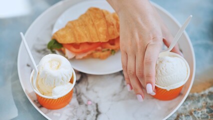 The girl takes the ice cream off the plate next to the croissant with the meat.