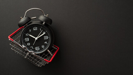 Black friday sales concept. Top view photo of black alarm clock in shopping cart on isolated black...