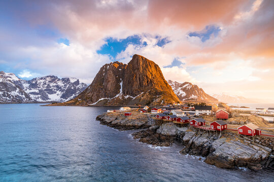 Clouds at sunrise over traditional Rorbu cottages on cliffs by the cold arctic sea, Hamnoy, Reine, Lofoten Islands, Norway