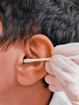 Ear wax cleaning with swab cotton bud sticks hisopo by ent specialist doctor with gloves on hands, earwax removal from teen boy's ear treatment closeup view image photo