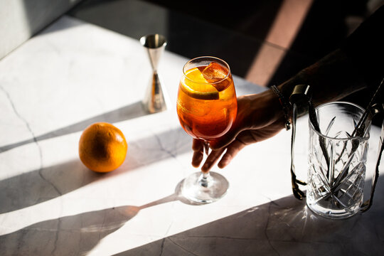 photography of a man's hand holding aperol spritz cocktail glass with orange slice 