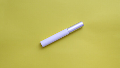 Rimel para ojos color blanco con tapa metalica sobre fondo amarillo. 
