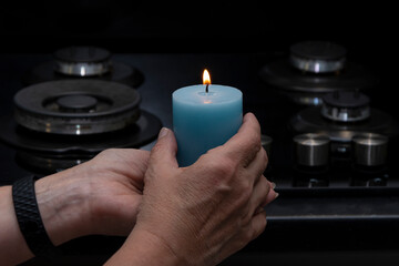 An elderly woman holds a burning candle in her hands, against the background of a non-working gas...