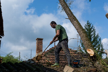 A man cleans the roof of a house after a big storm on a summer day. A man stands on the roof and...