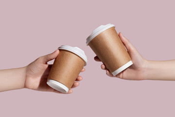 Women holding takeaway paper coffee cup on light pink background. Space for design. Mockup