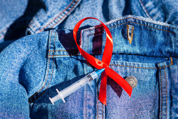 Red ribbon,syringe,needle,denim jacket. symbol HIV,AIDS cancer awareness and syringe outdoors shot on blurred nature background,Healthcare medicine sexually concept,World AIDS Day concept.