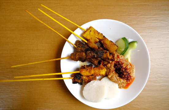 Flatlay picture of tripe, beef and chicken satay with "nasi impit", peanut sauce and vegetable on the table.