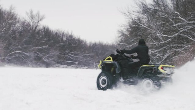 ATV Quad bike drifting on snow. Man on quad bike pulls in a yellow jacket woman on snowtube on frozen river at winter