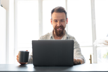 Stylish bearded man working on laptop from home sitting at the table