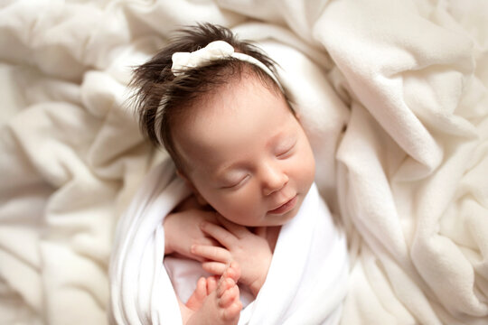 Top view of a newborn baby girl sleeping in a white cocoon on a white bed. Beautiful portrait of a little girl 7 days, one week. Macro studio professional photography.