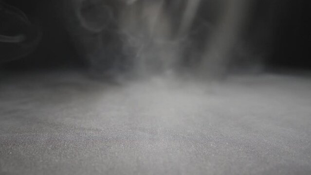 Close up of heavy white smoke from the vape spreading on the floor. Pure club of milk steam from an electronic cigarette or hookah covering on the surface. Black background. Low view Slow motion