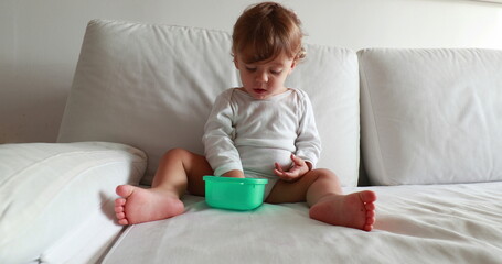Fototapeta premium Baby eating afternoon snack on couch. Calm one year old toddler boy resting on sofa