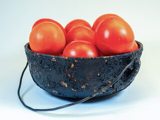 Studio shot of a very battered, burnt and old metalic pot with red tomatoes on a neutral background
