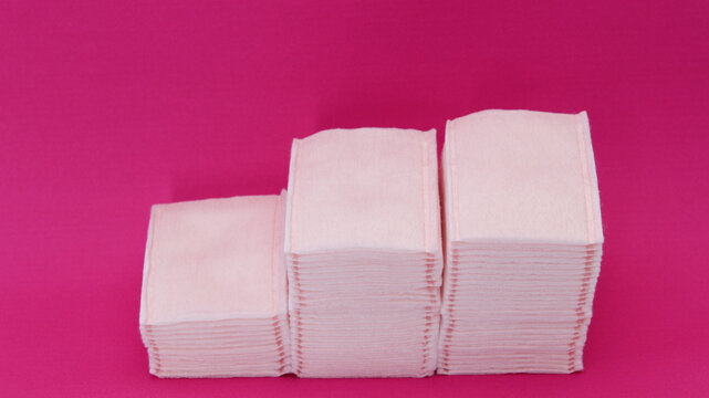 Almoadillas de algodon absorvente apiladas sobre un fondo rosa.