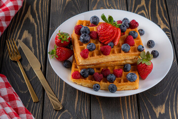 waffles with berries, strawberries and honey on wooden table