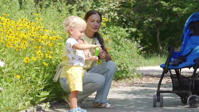 Happy mother and little child blowing soap bubbles in the park, kid and mom are playing on the nature outdoors.