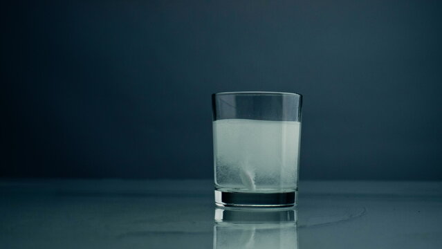 Tablet dissolving water glass at dark background closeup. Acid pill treatment