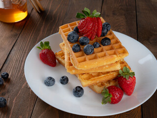 waffles with berries, strawberries and honey on wooden table