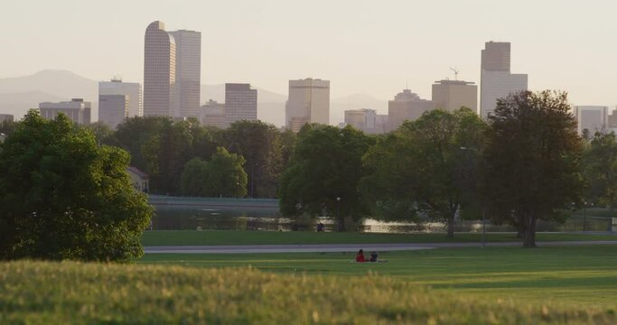Picnic goers in Denver grass park at sunset with downtown city view
