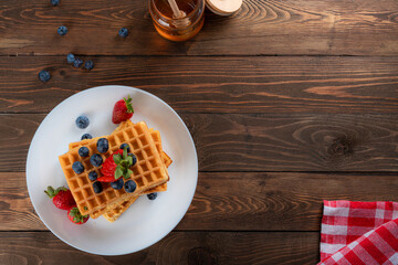 waffles with berries, strawberries and honey on wooden table