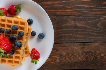 waffles with berries, strawberries and honey on wooden table