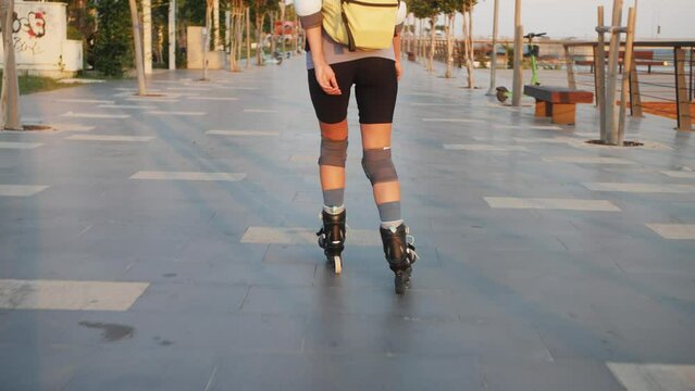 Following young sporty woman, rollerblading in the city with backpack.