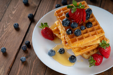 waffles with berries, strawberries and honey on wooden table