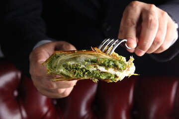 Oriental sweets. Pahlava with ice cream nuts, pistachio in a large dish on a black table with hands. Turkish dessert. Background image, copy space, horizontal