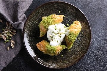 Oriental sweets. Pahlava with ice cream nuts, pistachio in a large dish on a black table. Turkish dessert. Background image, copy space, horizontal
