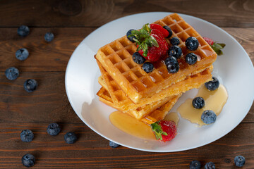 waffles with berries, strawberries and honey on wooden table