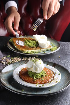 Oriental sweets. Pahlava with ice cream nuts, pistachio in a large dish on a black table with hands. Turkish dessert. Background image, copy space, horizontal