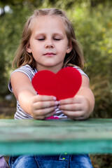 A child with a paper heart in his hands. Congratulations on Valentine's Day. copy space. Portrait of a cute little girl in the park outdoors. Love concept.