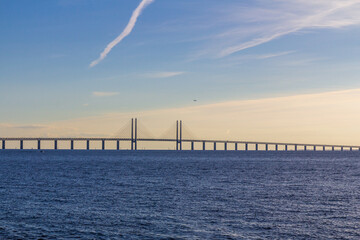 The Öresund bridge connecting Denmark and Sweden while a plane flies above it during summer sunset