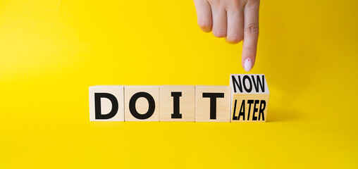 Do it now or later symbol. Businessman hand points at wooden cubes with words Do It Later and Do It Now. Beautiful yellow background. Business concept. Copy space