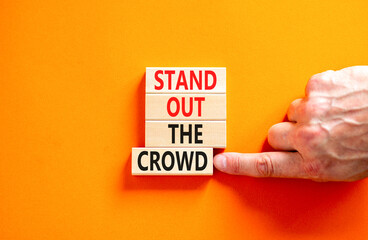 Stand out the crowd symbol. Concept words Stand out the crowd on wooden blocks on beautiful orange table orange background. Businessman hand. Business, stand out the crowd concept