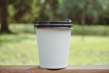 White disposable paper cup with plastic lid. A white paper cup. White paper cup for coffee on grass background. A white paper cup on the background of the street.
